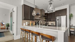A modern kitchen with a large island, bar stools, stainless steel appliances, and pendant lighting.