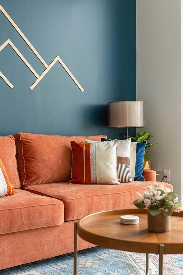 Een woonkamer met een bank, een lamp, een bijzettafeltje en een muur met geometrische decoratie.