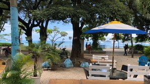 An outdoor seating area with tables and chairs, surrounded by trees and potted plants, overlooking a beach with the sea in the background. - Beautiful Costa Rican Villa in Gated Beach Resort (Playa Hermosa)