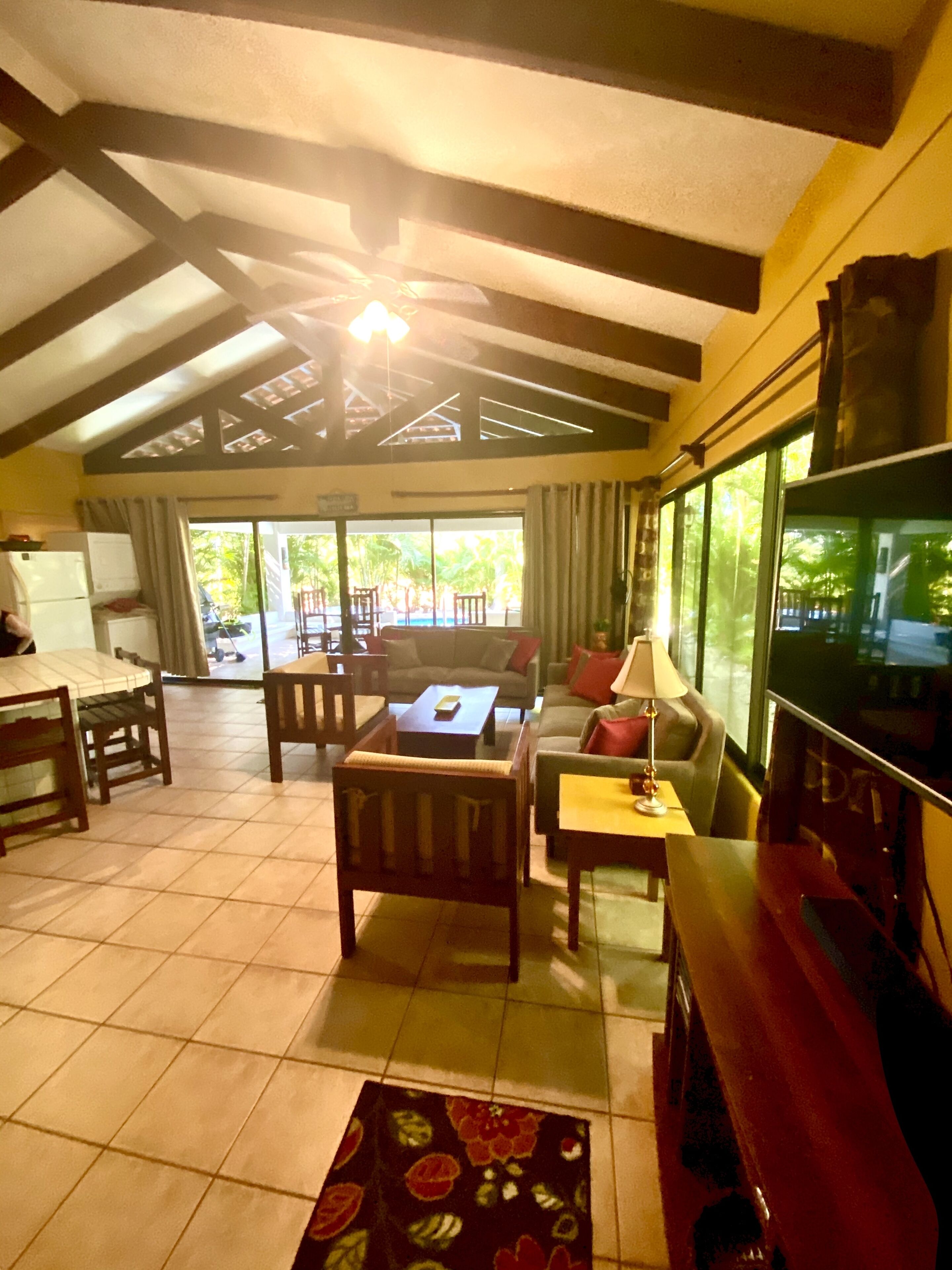 A spacious living area with a high ceiling, a television, and a view of the outdoors through large windows.