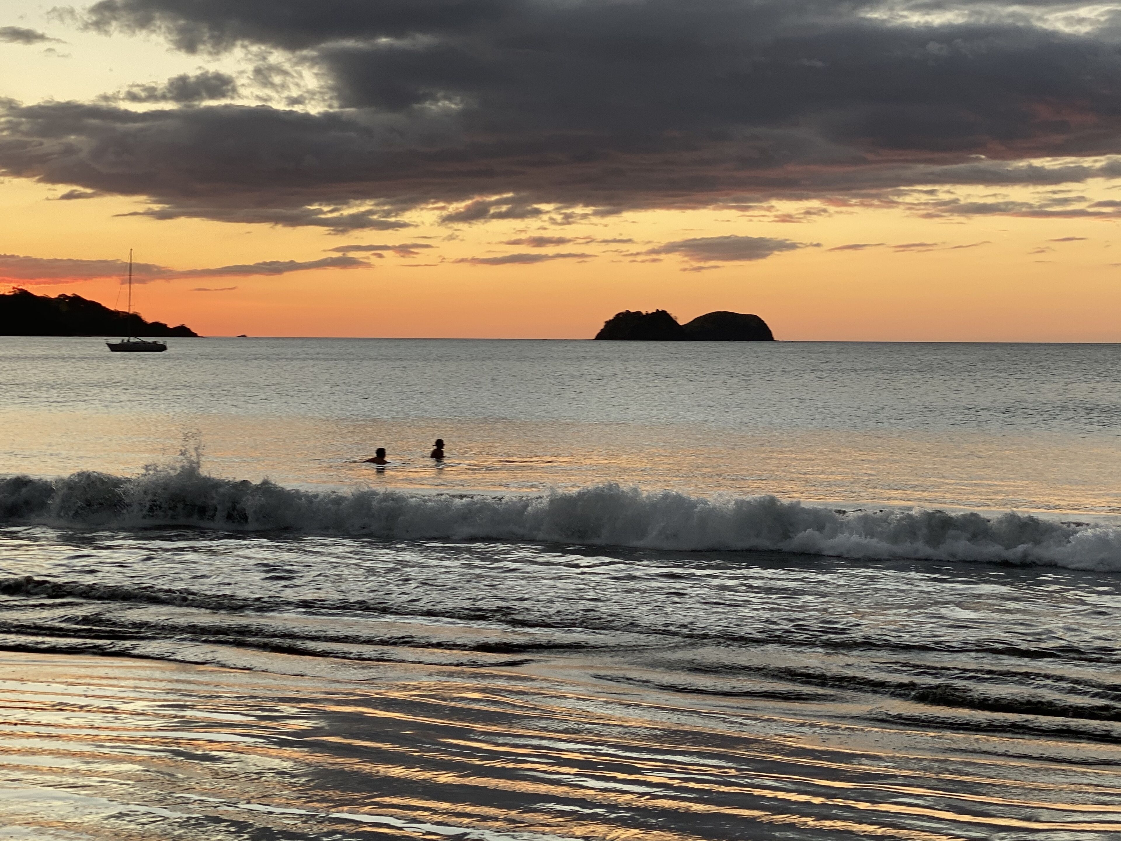 Uma praia com ondas, um barco e duas pessoas na água.