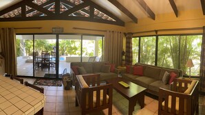 A spacious living area with a sofa set, a coffee table, and a television. There is a large window providing a view of the outdoors. - Beautiful Costa Rican Villa in Gated Beach Resort (Playa Hermosa)