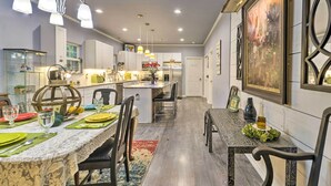 Una cucina moderna con mobili bianchi, un'isola centrale, illuminazione a sospensione e un'area pranzo con tavolo e sedie in marmo.