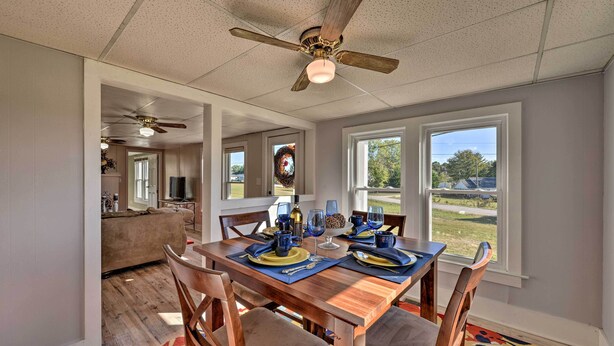 A dining area with a wooden table set for a meal, a ceiling fan, and large windows offering a view of the outdoors. - Porch, Fire Pit & Grill: Blue Ridge Mtn Cottage! (Hudson)