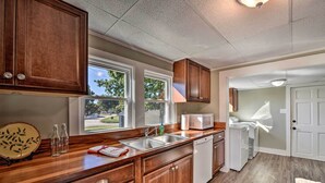 A kitchen with wooden cabinets, a stainless steel sink, and a dishwasher. There are windows providing natural light and a view of the outside. - Porch, Fire Pit & Grill: Blue Ridge Mtn Cottage! (Hudson)