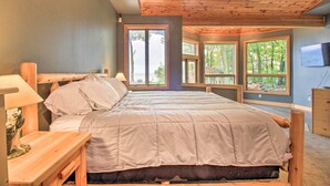 Une chambre avec un grand lit, une tête de lit en bois et un ventilateur de plafond. De nombreuses fenêtres offrent une vue sur l’extérieur.