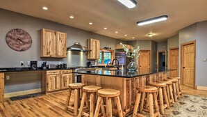 Une cuisine avec des meubles en bois, un grand îlot central doté de tabourets, une horloge et une fenêtre offrant une belle vue.