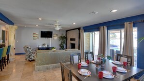 Un coin repas avec une table dressée pour quatre personnes, des chaises, un ventilateur de plafond et un téléviseur fixé au mur.