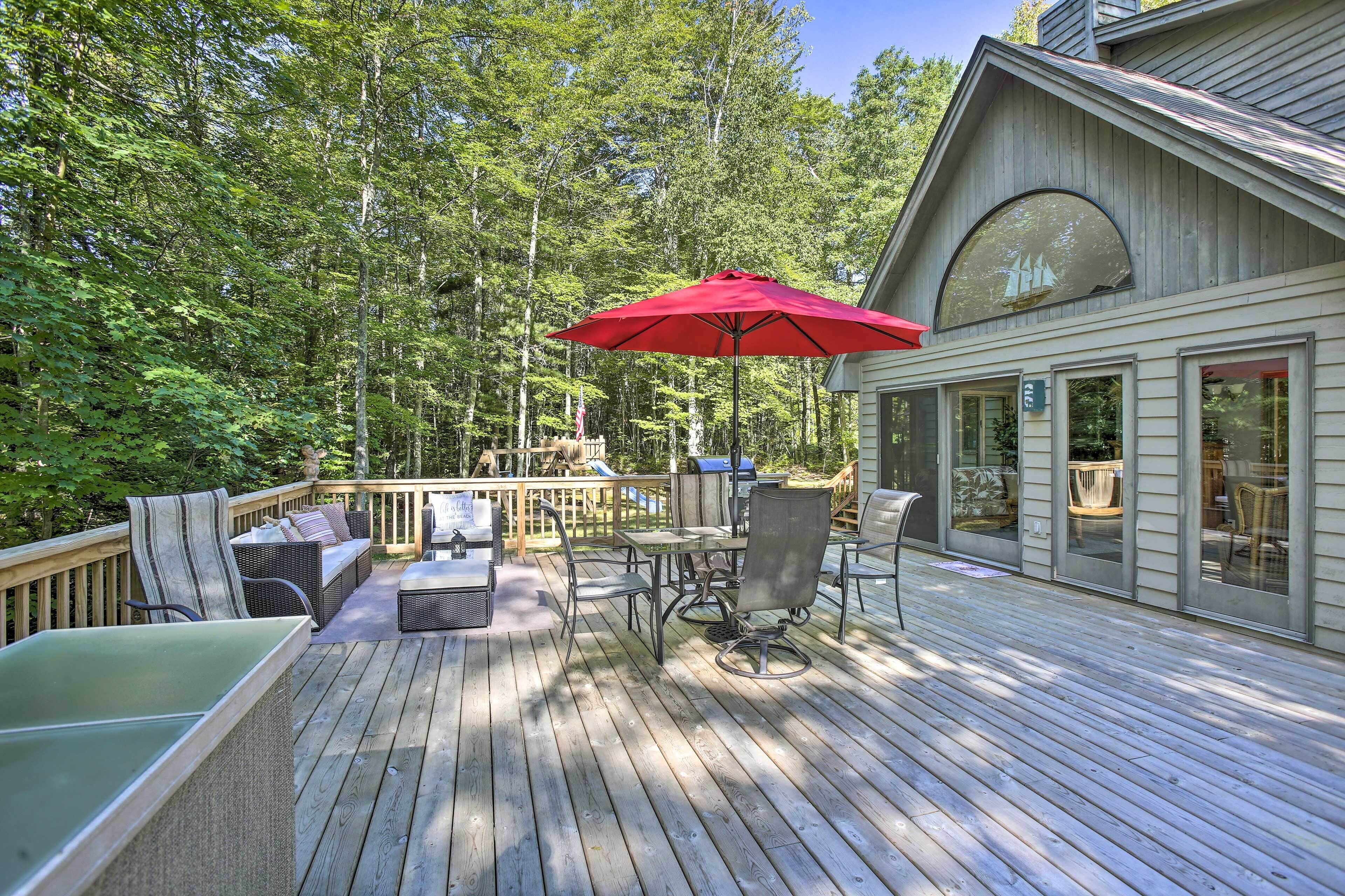 Une terrasse en bois avec des meubles d’extérieur, notamment un canapé et des fauteuils, ainsi qu’un parasol rouge.