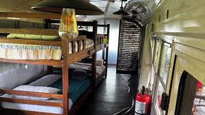 Un compartiment de train compact, équipé de lits superposés, d’une table avec des sets de table verts, d’un luminaire suspendu et d’un extincteur.