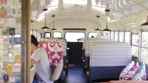 L'intérieur d'un autobus, avec des sièges à motifs, une allée centrale et un éclairage au plafond.
