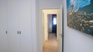 Een gang met een witte kast, een deur naar een andere kamer, en een schilderij van een strandzicht aan de muur.