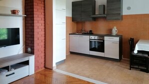A compact kitchen with a TV, a brick wall, and a dining area with a table and chairs.