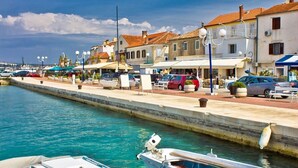 A marina with boats docked, a waterfront promenade, and buildings with red-tiled roofs.