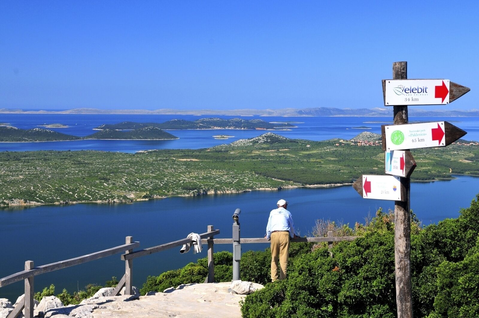 Un hombre está de pie sobre una plataforma de madera, contemplando un paisaje pintoresco bajo un cielo despejado.