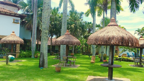 A courtyard with thatched umbrellas, palm trees, and outdoor seating areas. - OYO Pousada do Wagner, Rio das Ostras (Rio das Ostras)