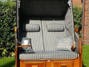 A striped outdoor lounge chair with cushions, a tray with a cup, and a wooden base.