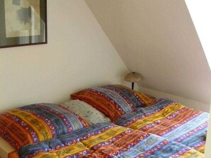 A bedroom with a sloped ceiling, a bed with patterned bedding, and a bedside lamp.
