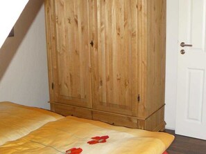 A bedroom with a wooden wardrobe, a bed with a yellow blanket, and a white door.