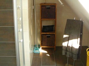 A bathroom with a shower, a towel rack, and a shelf with baskets.