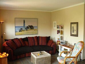 A living room with a sofa, a chair, a bookshelf, and a painting of a lighthouse.