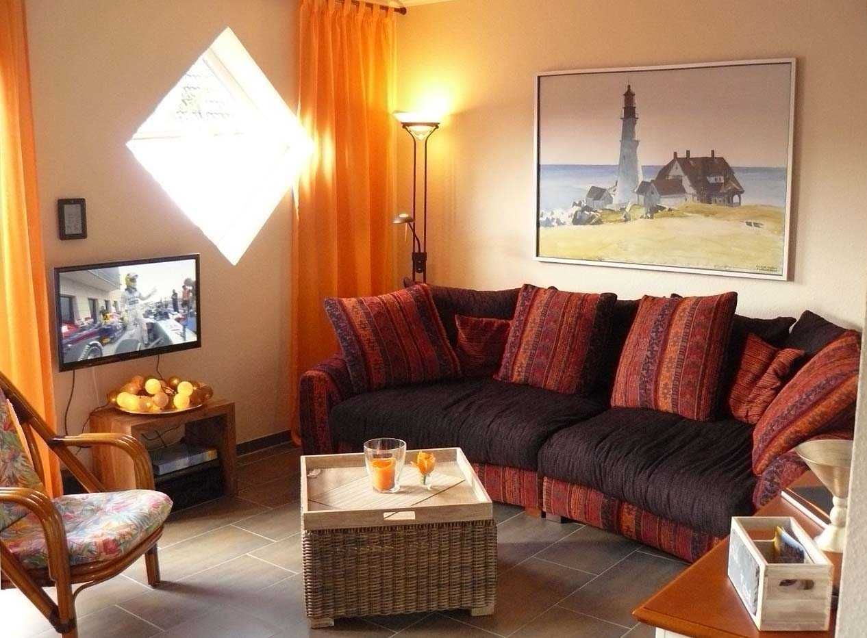 A cozy living room with a dark-colored sofa, a wicker coffee table, a television, and a painting of a lighthouse.