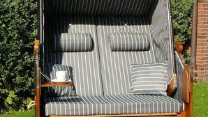A striped outdoor lounge chair with cushions, a tray with a cup, and a wooden base. - Vacation home Ambiente, Germany (Wittmund)