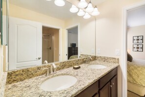 Une salle de bain avec deux lavabos, un grand miroir et une douche visible au fond.