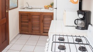 A kitchen with white tiles, wooden cabinets, a stove, and decorative items on the wall. - SIMI-HA-2BR-TULUM... (TULUM)