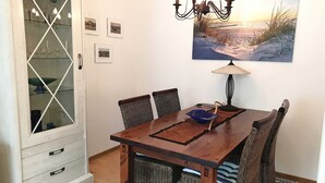 En matplats med ett träbord, flätade stolar, ett glasskåp och en tavla som föreställer en strandscen.