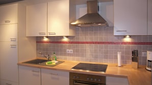 Eine moderne Küche mit weißen Schränken, einer Edelstahl-Dunstabzugshaube, einer Spüle mit zwei Becken und einem eingebauten Backofen.