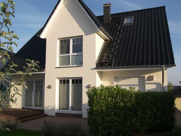 A two-story house with a gabled roof, a garage, and a well-maintained front yard with hedges.