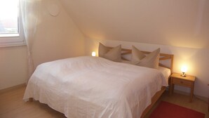 Ein Schlafzimmer mit einem Einzelbett, einem Nachttisch mit Lampe und einem Fenster mit Vorhängen.