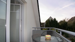 Ein Balkon mit einem Glastisch, zwei Korbstühlen und einer bunten Schale.