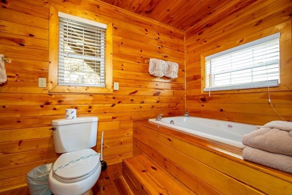 A wooden cabin bathroom with a toilet, sink, and bathtub.