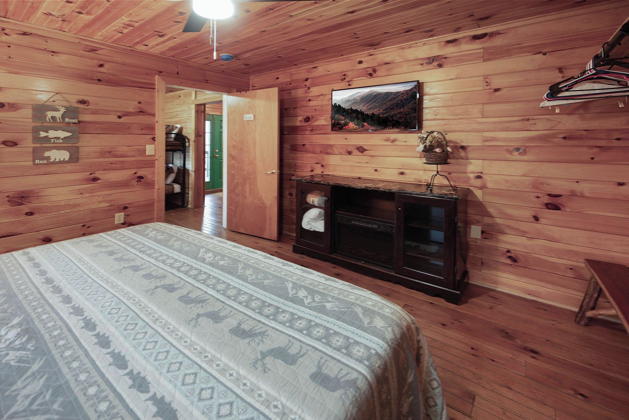 A wooden cabin room with a bed, a fireplace, and a door leading to another room.