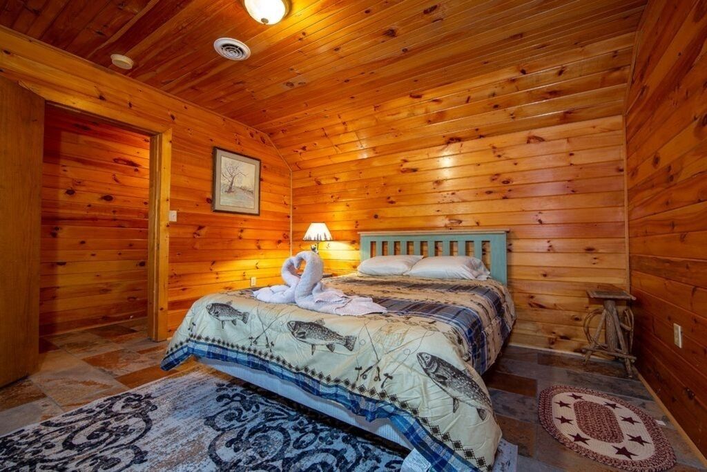 Ett sovrum i en stuga med träpanel, inrett med en säng, ett nattduksbord, en lampa och en inramad tavla på väggen.
