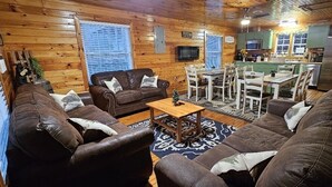 A cozy cabin interior with a living room, dining area, and kitchen. -  Smoky Mtn Hideaway - 7BR, Hot Tub +Movie Theatre + Darts+ Firepit+ Pets ok (Sevierville)