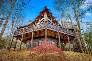 Une cabane dotée d’une terrasse en bois, de grandes fenêtres et d’une cheminée en pierre.