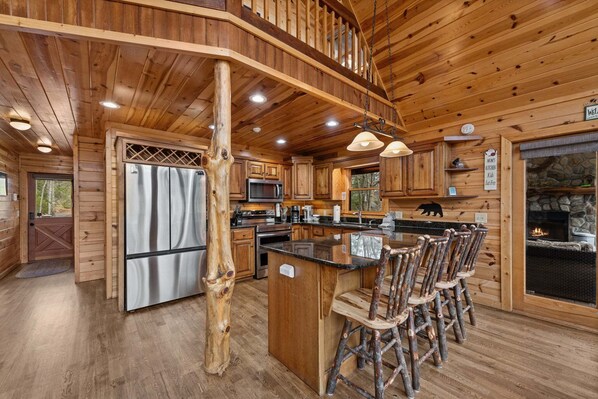A wooden cabin interior with a kitchen, bar area, and a stone fireplace.