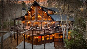 A cabin with a deck, large windows, and a stone chimney.