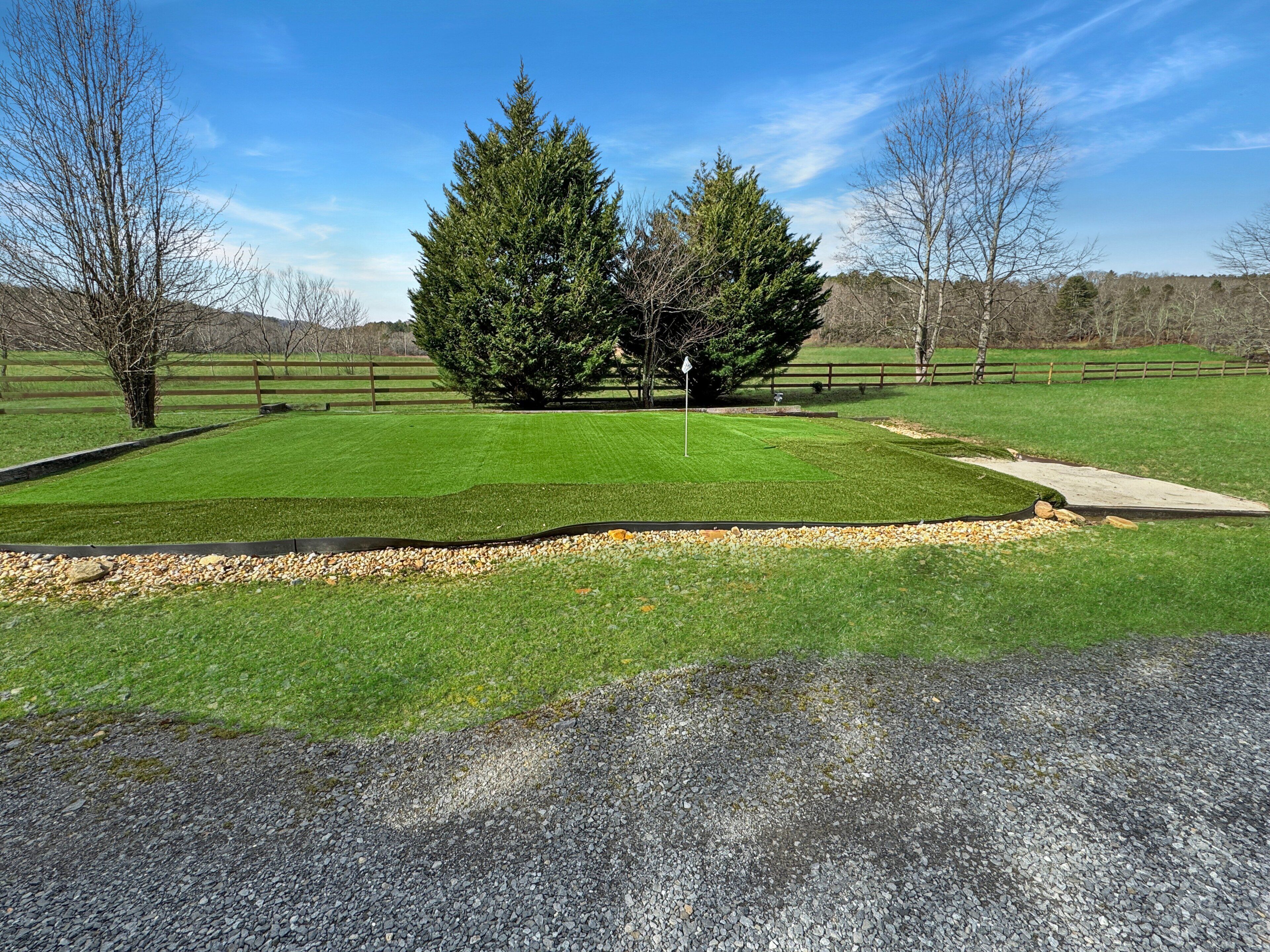 A well-maintained grassy area with a gravel path, surrounded by trees and a wooden fence.