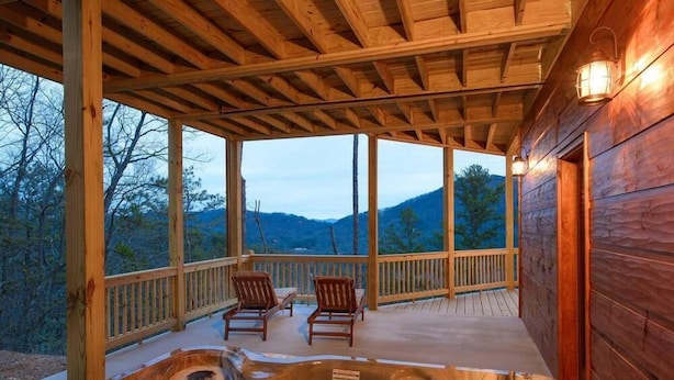 Una terraza de madera con un jacuzzi, dos sillas y vistas a montañas.