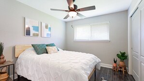 A bedroom with a bed, a ceiling fan, a window with blinds, and a small table with plants. - New Remodel Modern Decor 2 Minutes to Restaurants Mall of LA Target I-10 TopGolf (Baton Rouge)