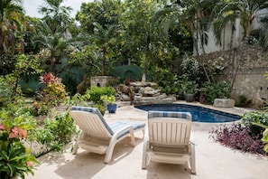 A pool area with two lounge chairs and a stone wall.