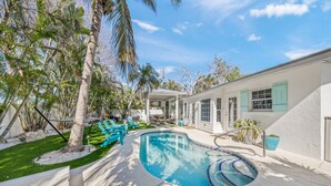 A swimming pool with a curved design, surrounded by palm trees and a patio area with outdoor furniture.