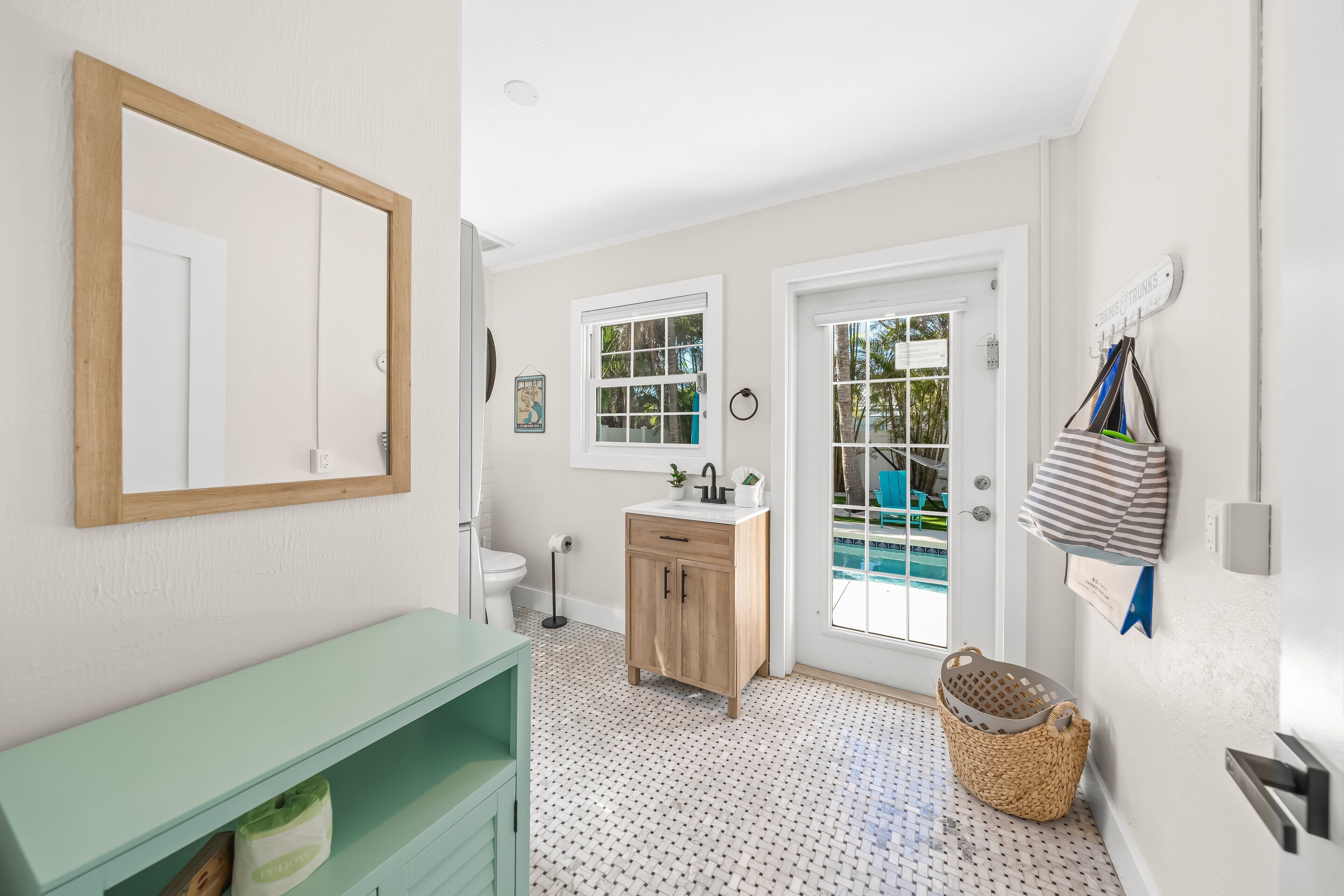 A bathroom with a wooden cabinet, a sink, a mirror, and a door leading to a pool area.