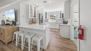 A modern kitchen with white cabinetry, a central island with bar stools, and a fire extinguisher mounted on the wall.