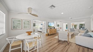 A spacious living area with a white ceiling fan, a dining table with chairs, a sofa, and a television.