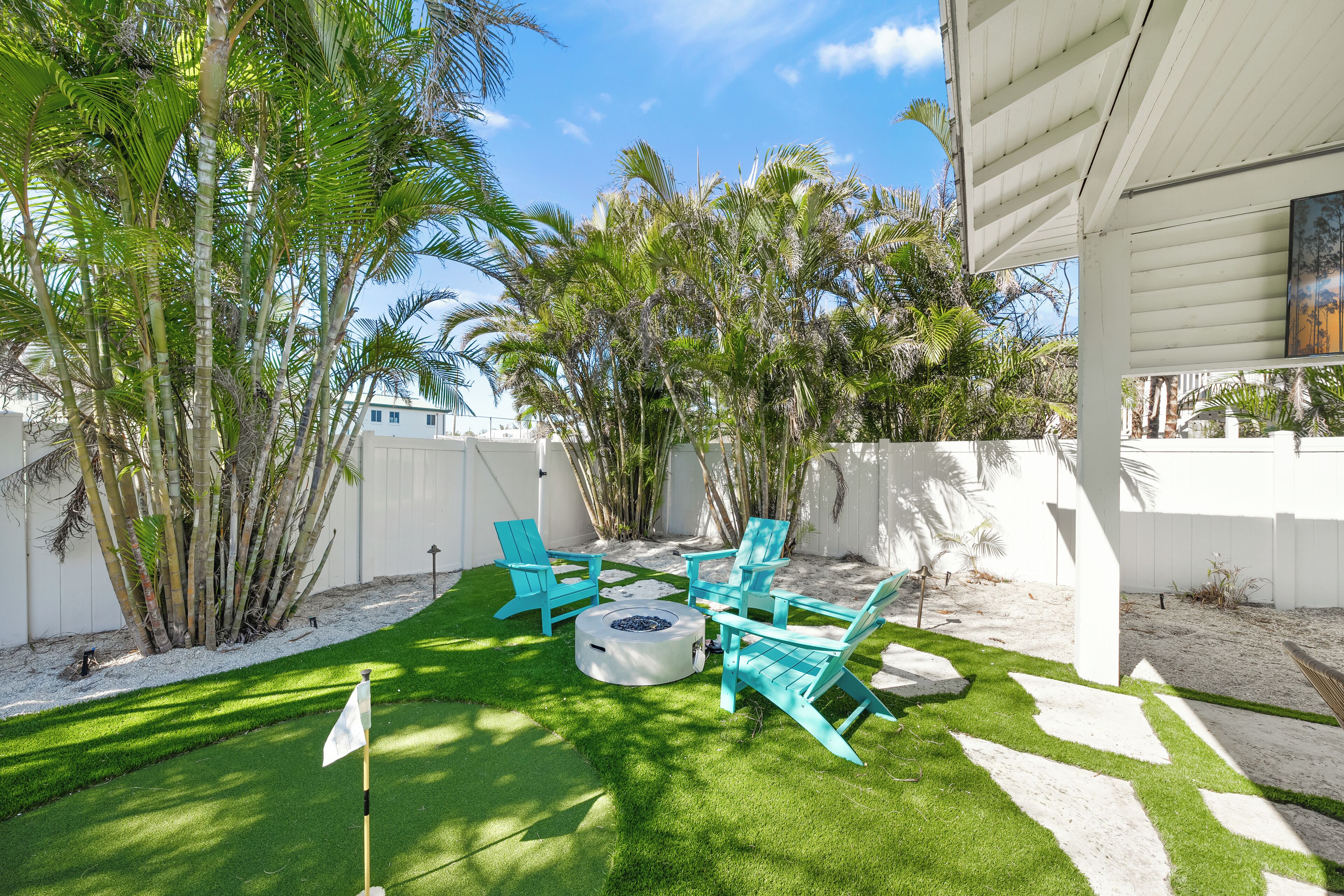 A backyard with a fire pit, turquoise chairs, and a flag on the grass.